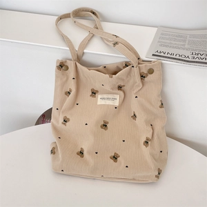 Detail of beige corduroy tote bag featuring embroidered bear patterns and soft texture