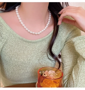 Close-up of elegant single-strand pearl necklace on model in green knit sweater