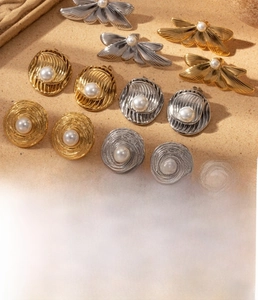 Detail of titanium steel pearl earrings with dragonfly motif and spiral textures in gold