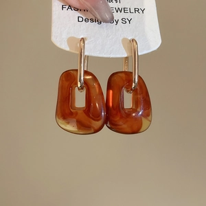 Detail of amber acrylic square pendant and golden metal hoop with natural textures