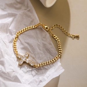 Gold Cuban link bracelet with zircon cross charm on white textured background
