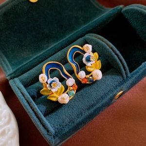 Close-up of vintage floral drop earrings with blue enamel and pearls on green velvet