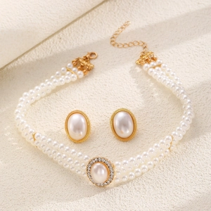 Parure collier perles à trois rangs et boucles d'oreilles dorées sur tissu beige texturé