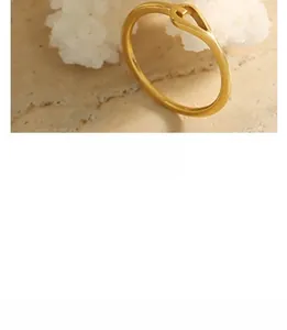 Gros plan d'une bague dorée torsadée minimaliste sur fond de corail blanc et de pierre