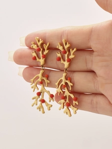 Detailed view of gold coral branch earrings with red beads held by hand for scale