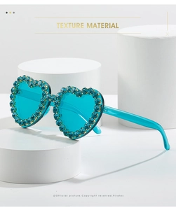 Close-up of heart-shaped sunglasses with blue rhinestones on a white display pedestal