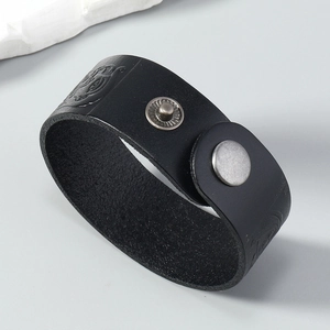 Detail of black wide leather bracelet with embossed skull pattern and silver metal snap