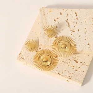 18K gold plated stainless steel sunburst earrings on a beige travertine stone base