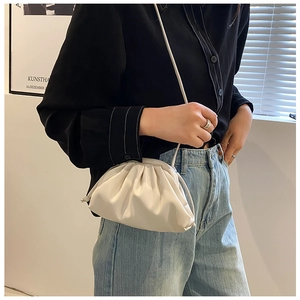 Close-up of a cream white ruched dumpling bag with a slender leather shoulder strap
