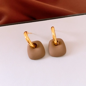 Close-up of matte brown square pendant on golden C-shape earrings with textured background