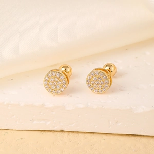 Detail of round gold ear studs with pavé-set zircons on a textured stone surface