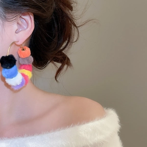 Close-up of oversized gold hoop earrings with multi-colored plush pom-pom design