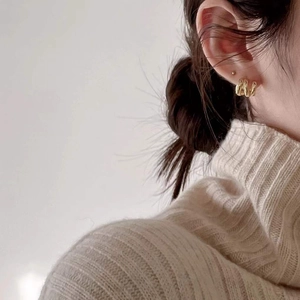 Detail view of triple layered gold hoop earrings worn with a beige sweater