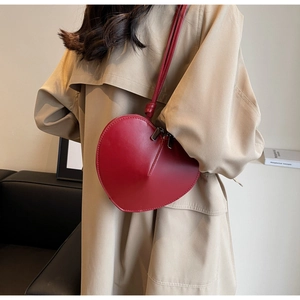 Dettaglio di una borsa a tracolla rossa a forma di cuore abbinata a un trench beige