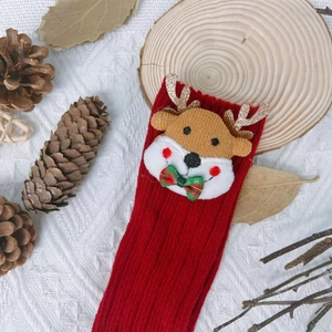 Festive red knitted Christmas socks for babies featuring a cute reindeer plush doll