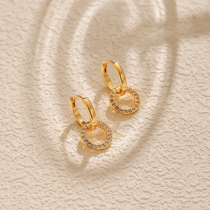 Macro shot of gold hoop earrings with sparkling white zircon charms on a textured background