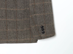 Detailed view of herringbone tweed sleeve with orange plaid and three black buttons