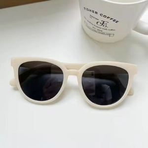 Detail view of cream-colored wide-frame sunglasses with dark lenses on a white background