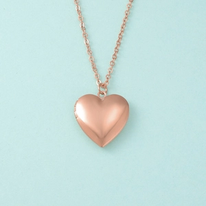 Macro detail of rose gold heart locket necklace with hinge on light blue background