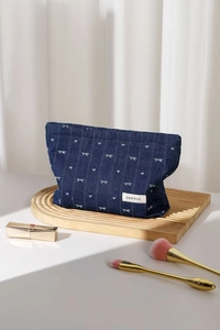 Detail of denim bow makeup bag on wooden shelf with lipstick and brushes
