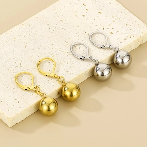 Close-up of polished gold and silver oval ball earrings on a stone display stand