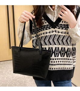 Detail of black crocodile embossed tote bag with sturdy handles on a stylish model