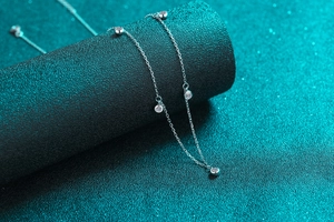 Macro shot of S925 sterling silver chain with moissanite bubble charms on green texture
