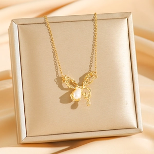 Elegant gold butterfly necklace with teardrop pearl and zircons on a beige silk background