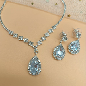 Detailed view of silver necklace and teardrop zircon earrings on pink tulle background