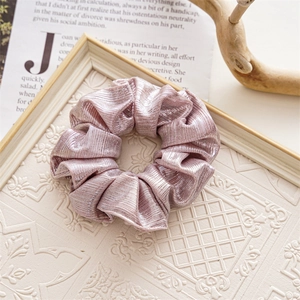 Close-up of a pink metallic pleated hair scrunchie on a vintage white relief tray