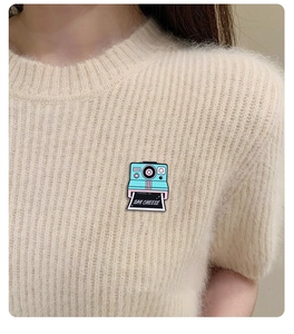 Teal enamel camera brooch with Say Cheese photo pinned on a beige knit sweater