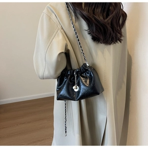 Detail of black pleated cloud bag with pearl charm and chain strap worn by model