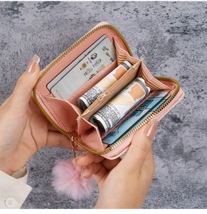 Portafoglio trapuntato rosa con pompon e fessure per carte su sfondo di marmo