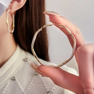 Close-up of gold metal hoop earrings with white enamel ripple texture on model