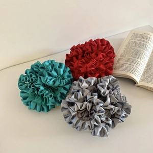 Close-up of three satin pleated flower hair ties in green, red, and silver grey finishes
