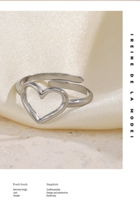 Close-up of a silver open heart ring on white satin fabric with a minimalist aesthetic