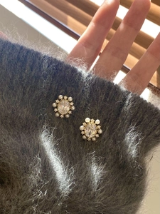 Detailed view of flower earrings with pearls and oval zircon on a cozy grey sweater