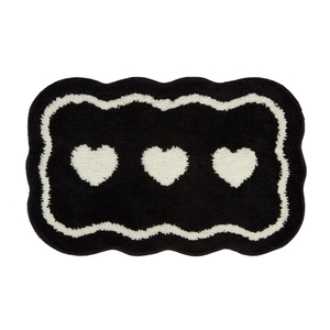 Thick plush black bathroom mat with three white hearts and wavy edges on white background