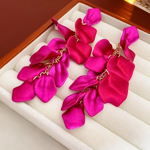Détail de boucles d'oreilles pétales rouge givré avec pompons dorés sur velours