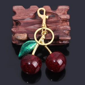 Close-up of glittery red cherry keychain with green leaf on gold metal clasp and ring