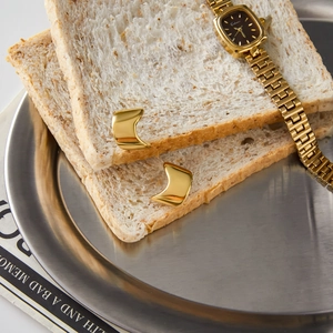 Detailed view of polished golden C-shaped stud earrings placed on a breakfast toast