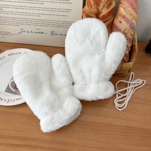 Close-up of white faux fur mittens with hanging cord on a rustic wooden table background