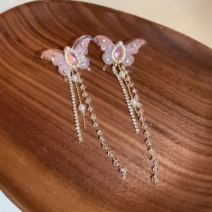 Close-up of pink butterfly earrings featuring long rhinestone tassels and pearl accents