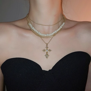 Detail of layered gold necklace with pearl strands and a vintage cross pendant on model
