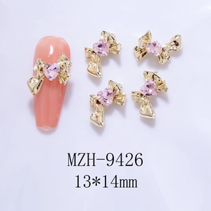 Detail of gold bow nail charms with pink heart gems sized 13x14mm on a manicure