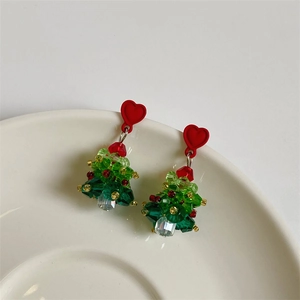 Detailed view of handmade crystal beaded Christmas tree earrings hanging on a white bowl