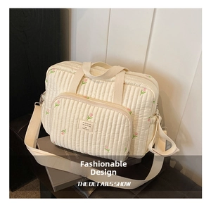 Detail of cream quilted diaper bag with pink floral embroidery and multiple zipper pockets