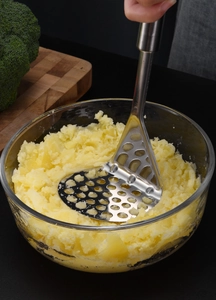 Gros plan d'un presse-purée en inox écrasant des pommes de terre dans un bol en verre