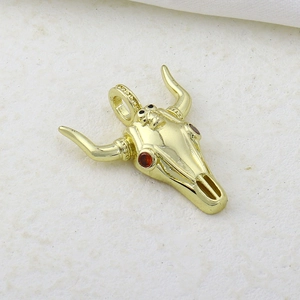Detailed close-up of golden bull skull pendant with red gemstone eyes on textured background