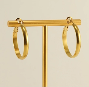 Golden matte hoop earrings showcased on a T-shaped jewelry display stand with a warm background